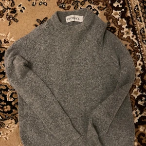 Grå stickad tröja från Ivyrevel - Mysig grå stickad tröja från Ivyrevel med hög hals och långärmad design. Tröjan är tillverkad i en mjuk blandning av polyamid, akryl, mohair, ull och elastan som ger en skön och fluffig känsla. Perfekt för kyliga dagar och enkel att matcha med jeans eller kjol.