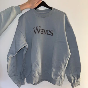 Ljusblå sweatshirt från Vailent Waves - Sweatshirt i ljusblå färg från Vailent med trycket 'Waves' på bröstet. Tröjan har rund hals, ribbade muddar och är tillverkad i mjuk ekologisk bomull. Passformen är loose och den har långa ärmar.