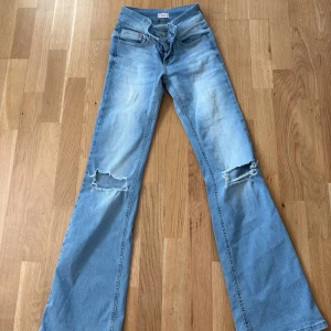 Bootcut jeans med hål knäna från Nelly - Snygga ljusblå bootcut jeans från Nelly med slitna detaljer på båda knäna. Modellen har klassisk femficksdesign och är tillverkad i mjukt denimtyg. Perfekt för dig som gillar en avslappnad och trendig look.