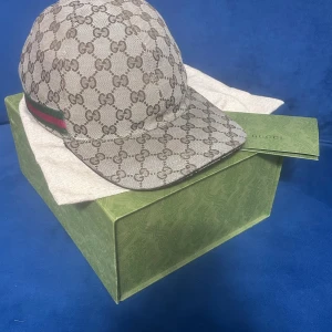 Gucci keps beige  - Gucci keps i beige. Jag vill nu sälja min Gucci keps i beige som är använd men i toppform. Jag har behandlat den här kepsen nästan som mina barn den är väl omhändertagen! Kvittot och allt som följde med vid köpet finns kvar och ingår vid försäljningen. Kepsens nuvarande pris ligger runt 5000 kr. Storleken är L, men den passar även M eftersom den kan justeras baktill.