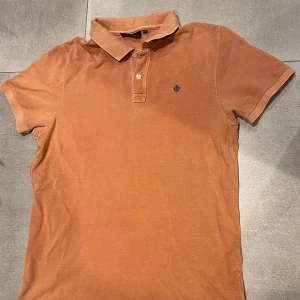 Morris piké  - Säljer en brun/orange piké  från Morris med klassisk krage och två knappar framtill. Tröjan har korta ärmar och en liten broderad logga på bröstet. Perfekt för en avslappnad men ändå stilren look. Passar perfekt nu på hösten med färgen och så vidare. Storlek L och skicket är mittemellan det är ett litet hål (se på bild) och sen är kragen lite urtvättad! Hör av dig vid minsta lilla fundering mvh em_resell