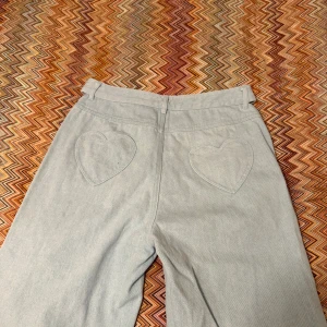 Ljusblå wide jeans med hjärt-fickor från Cloeys - Supersnygga ljusblå jeans från Cloeys  med breda ben och hjärtformade bakfickor. Byxorna har hög midja och klassisk jeanslook, perfekta för dig som vill sticka ut lite extra. Materialet är jeans och passformen är loose och wide.