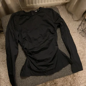 Svart figursydd topp från ZARA -  Svart långärmad topp från ZARA med figurnära passform. Toppen har rynkningar på sidan. Storlek Xs. Använd 1 gång.