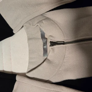 Stickad klänning från Tiger of Sweden - Supersnygg stickad klänning från Tiger of Sweden i grått och svart. Modellen är figurnära med lång ärm och cool dragkedja framtill. Klänningen har kontrastfärgade detaljer på ärmar och nederkant som ger en modern look. Perfekt för dig som gillar stilrena vibes.