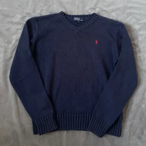 Marinblå stickad tröja Polo Ralph Lauren | S - Säljer en marinblå stickad tröja från Polo Ralph Lauren i storlek S. Tröjan har v-ringning, långa ärmar och ribbade muddar. Klassisk röd broderad logga på bröstet. Perfekt för dig som gillar stilren och tidlös design.