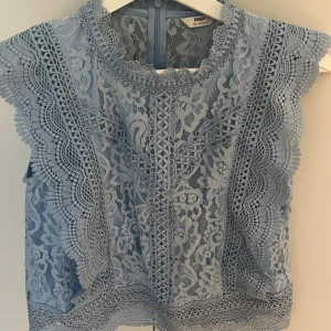 Blå spetsblus från ONLY - Supersöt ljusblå blus från ONLY i spets med blommigt mönster och fina detaljer längs kanterna. Ärmlös modell med rund halsringning och dragkedja i ryggen. Perfekt för dig som gillar romantisk och feminin stil.