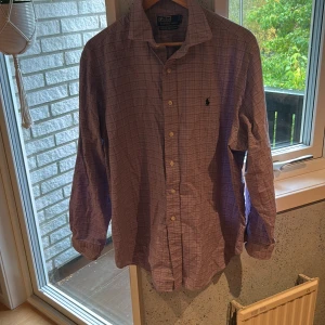 Lila rutig skjorta från Polo Ralph Lauren - Snygg Ralph lauren skjorta i storlek L, men skulle säga att den passar mer som M. Den är i bra skick. Hör av er vid funderingar.