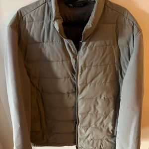 Grå quiltad pufferjacka från Zara XL - Snygg grå pufferjacka från Zara i storlek XL. Jackan har quiltad design, dragkedja framtill och två sidofickor. Materialet är polyester och jackan har en stilren, enkel look som passar perfekt till kyligare dagar.
