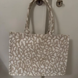 Beige shoppingväska med leopardmönster - Stor och rymlig shoppingväska från H&M i beige och vitt med leopardmönster. Väskan har två rejäla handtag och ett stort fack med innerficka som stängs med dragkedja. 