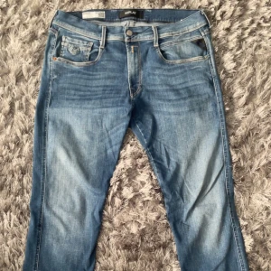 Replay Anbass Hyperflex jeans blå 34 / 34 - Snygga Replay Anbass Hyperflex jeans i klassisk blå tvätt. Modellen har fem fickor, smal passform och stretchigt denimtyg för extra komfort. Perfekta för dig som gillar stilrena och moderna jeans med lite slitningar. Hör av er om ni har frågor, priset kan diskuteras vid snabb affär!