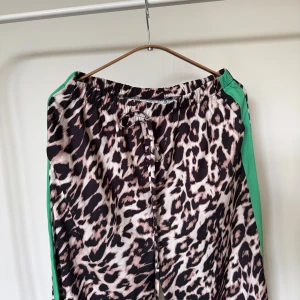Leopardmönstrade byxor med gröna revärer  - Byxor med leopardmönster och gröna sidorevärer. Byxorna med snörning och är tillverkade i ett mjukt, skönt material. 