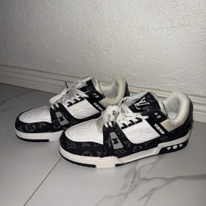 Louis Vuitton svartvita sneakers - Svartvita Louis Vuitton sneakers med klassiskt monogrammönster och tydliga LV-loggor på tunga och häl. Skorna har snörning, platt sula och rund tå. Materialet är en mix av skinn och textil, med snygga kontraster mellan svart och vitt. Skorna är aldrig använda utan har bara stått i garderoben, så helt nya! 