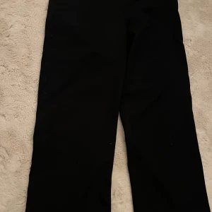 Svarta raka kostymbyxor - Snygga svarta kostymbyxor med rak passform och klassisk midja. Byxorna har en stilren design utan synliga detaljer och är perfekta för en clean look. Materialet känns mjukt och har en lätt stretch, vilket gör dem bekväma att bära hela dagen.