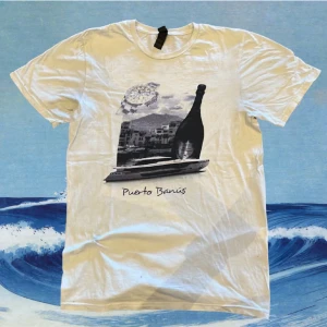 Puerto Banús t-shirt med tryck - Snygg vit t-shirt med stilrent tryck på framsidan som visar en klocka, champagneflaska, yacht och texten 'Puerto Banús'. Klassisk rund hals och korta ärmar, perfekt för chill dagar. Materialet är mjuk bomull.