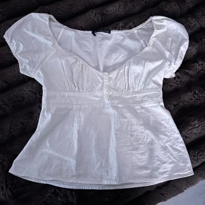  Brandy Melville top - Supersöt vit top från Brandy Melville med korta puffärmar, v-ringning och knappar framtill. Blusen har en lätt utsvängd passform och är gjord i ett tunt, mjukt bomullstyg med diskret struktur. Använd fåtal gånger 🤍 passar S/M