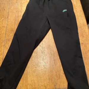 Svarta mjukisbyxor från Lacoste - Svarta mjukisbyxor från Lacoste med klassisk krokodillogga på höger sida. Byxorna har elastisk midja med snörning och är tillverkade i mjukt material som känns skönt mot huden. Passformen är loose och de har raka ben för en chill look. Helt nya fick dom och va fel storlek passar M och S, kan gå ner vid snabb affär