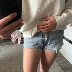 Ljusblå denimshorts med rå kant - Säljer ett par ljusblå jeansshorts med fransig, rå kant och klassisk femficksdesign. Shortsen har en normal passform och är tillverkade i bomull. Perfekta för varma dagar och har en avslappnad vibe.