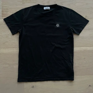 Svart T-shirt från Stone Island - Säljer en snygg T-shirt från Stone Island i svart färg och logga på bröstet. T-shirten är i storlek M