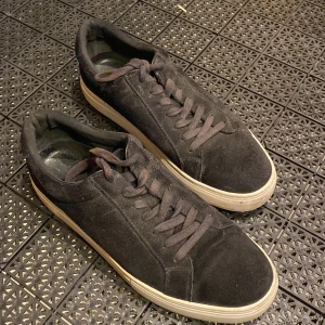 Svarta mockasneakers från Vagabond - Svarta sneakers från Vagabond med ovandel i mjuk mocka och platt vit sula. Skorna har rund tå, snörning och diskret design som passar till jeans eller chinos. Insidan är fodrad med skinn för extra komfort. Perfekt för dig som gillar stilrena och klassiska sneakers. (Sparsamt använda)