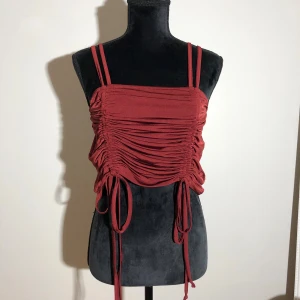 Vinröd croppad topp - Snyggt linne som aldrig blivit använd. Knytdetaljerna fram går att justera. Längd ca 45cm. Pris: 10kr 