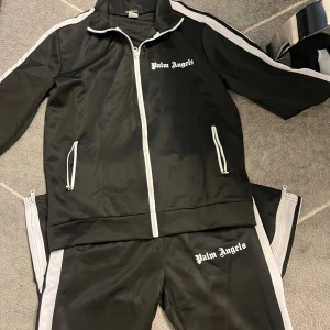 Svart vindjacka från -  svart vindjacka med vita detaljer och dragkedja framtill. Jackan har vita ränder längs ärmarna, ståkrage och två fickor med vita dragkedjor. Materialet är syntet och jackan har en sportig vibe med logotyp på bröstet.