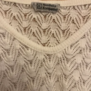 Vit stickad tröja från Nordiska Kompaniet - Supersöt vit stickad tröja från Nordiska Kompaniet med lång ärm och vackert spetsliknande mönster. Tröjan har v ringning och ribbade muddar. Perfekt för lager-på-lager och ger en fräsch och stilren look. Jättefin till ett par jeans! Och något smycke. 