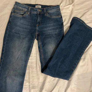 Blå bootcut jeans från ONLY - Snygga blå bootcut jeans från ONLY med klassisk femficksdesign och lätt slitning på låren. Storlek S/ 30. Jeansen har normal midja och är tillverkade i ett mjukt denimtyg med lite stretch för extra komfort. Perfekta för dig som gillar en retroinspirerad look. 