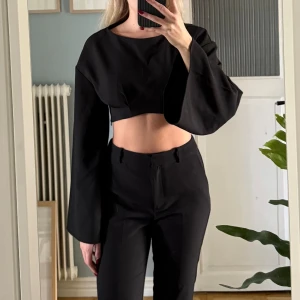 Svart croppad topp med vida ärmar - Säljer en svart croppad topp från NA-KD med riktigt vida och långa ärmar. Toppen har en rund halsringning och är tillverkad i ett mjukt bomullsmaterial. Perfekt för dig som gillar en edgy och modern stil med fokus på siluett.