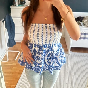 Vit och blå tubtopp - Supersöt tubtopp i vitt med blått broderat mönster. Toppen sitter tajt över bysten med resår och en gummikant som håller upp toppen bättre (skriv för bilder!).  Köpt i somras från en butik i Grekland!