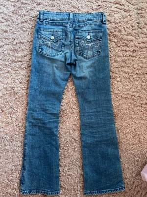 Blå bootcut jeans Gina Tricot 158 - Säljer ett par blå bootcut jeans från Gina Tricot i storlek 158. Jeansen har klassisk femficksdesign, snygga broderade detaljer på bakfickorna och silverfärgade knappar. Tillverkade i jeansmaterial med en lätt tvättad look.