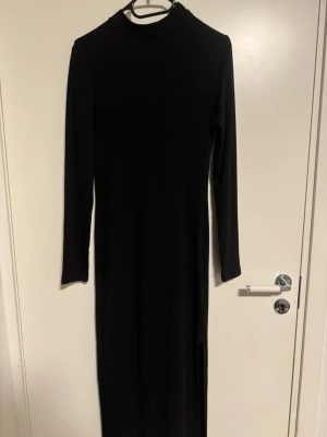 Svart långärmad långklänning från stradivarius  - En svart, ribbad långklänning med lång ärm och hög hals. Klänningen har en enkel och stilren design, perfekt för dig som gillar minimalistiskt mode. Materialet känns mjukt och stretchigt, vilket gör den bekväm att bära hela dagen.