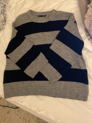 Randig grå och svart stickad tröja - Mysig stickad tröja från Lager 157 i grått och svart med breda ränder. Klassisk rund halsringning och långa ärmar. 