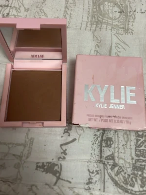Kylie Jenner bronzer Tanned and Gorgeous - Säljer en Kylie Jenner Pressed Bronzing Powder i nyansen 400 Tanned and Gorgeous. Kommer i en snygg ljusrosa fyrkantig dosa med spegel. Pudret är varmt brunt och ger en solkysst look. Förpackningen är rosa med silvrig text.