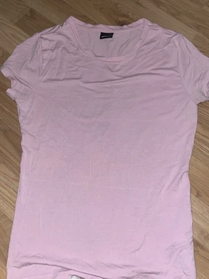 Ljusrosa basic t-shirt från Gina Tricot - En enkel och mjuk ljusrosa t-shirt från Gina Tricot. Klassisk rund halsringning och korta ärmar. Perfekt att matcha med jeans eller kjol för en clean look. Tillverkad i tunn bomull som känns skön mot huden.