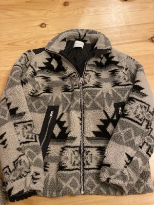 Mönstrad teddyjacka från Vailent - Säljer en grå och svart teddyjacka från Vailent med grafiskt mönster. Jackan har dragkedja framtill, två fickor med dragkedja och hög krage. Perfekt för kyliga dagar och riktigt skön att mysa i. Nypris 800kr knappt använd. Inga tecken på användning