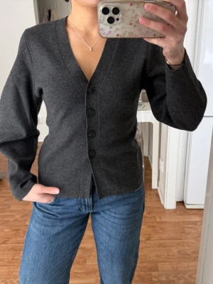 Mörkgrå figursydd kofta från H&M - mörkgrå snygg figursydd kofta från H&M i storlek XS. Koftan har v-ringning, fyra knappar framtill och är långärmad. Så perfekt kofta som tyvärr inte kommit till användning