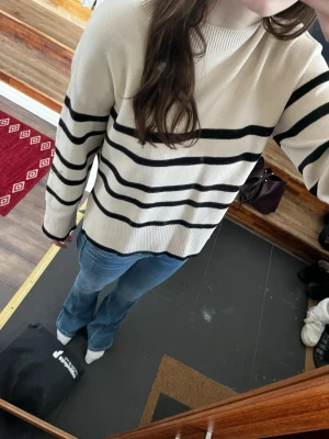 Randig vit och svart stickad tröja - Säljer en vit stickad tröja med svarta horisontella ränder. Tröjan har rund halsringning, lång ärm och en relaxed, lite loose passform. Perfekt till jeans för en enkel och snygg look.