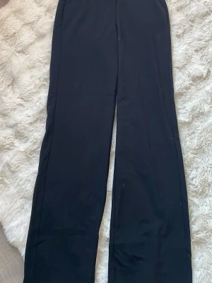 Svarta kostymbyxor First Class Collection - Snygga svarta kostymbyxor från First Class Collection i storlek 34. Byxorna har raka, vida ben och klassisk passform. Perfekta till en stilren look och passar till många olika outfits. Materialet känns mjukt och följsamt. Pris 50kr