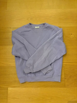 Ljuslila sweatshirt från Gina Tricot - En basic ljuslila sweatshirt från Gina Tricot, basically basics-kollektionen. Tröjan har rund hals, ribbade muddar och är långärmad. Perfekt för chill dagar och enkel att styla med jeans eller mjukisbyxor. 70% Bomull, 30% Polyester.