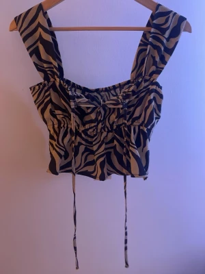 Zebramönstrad topp från ONLY - Snygg croppad topp från ONLY med breda axelband och zebramönster i svart och beige. Toppen har snörning framtill och är tillverkad i ett lätt och luftigt material, perfekt för varma dagar. Pris går att diskuteras💗