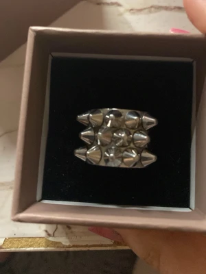 Silvrig ring med nitar från Edblad - Säljer en chunky ring från Edblad i blankt silverfärgat metall med coola konformade nitar runt halva ringen. Strl 16.80mm OBS KOMMER EJ MED LÅDA 