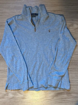 Grå half zip tröja Polo Ralph Lauren - Snygg ljusgrå långärmad tröja från Polo Ralph Lauren med klassisk broderad logga på bröstet. Tröjan har en half zip-dragkedja och hög krage, perfekt för lager på lager. Tillverkad i mjuk bomull för skön känsla hela dagen.