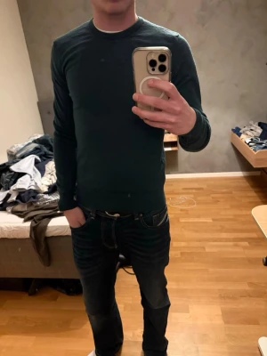 Mörkgrön stickad tröja från J.Lindeberg - Snygg mörkgrön stickad tröja från J.Lindeberg med rund hals och ribbade muddar. Perfekt passform som sitter normalt och långa ärmar. Stilren design utan mönster, passar dig som gillar enkelhet och kvalitet.