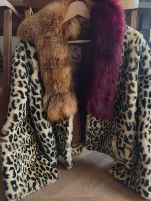 Leopardmönstrad pälsjacka med krage - Unik leopardmönstrad pälsjacka från något tyskt märkte tror jag. Bred krage i brun och mörkröd päls. Jackan har en loose passform och är perfekt för dig som vill sticka ut. Fodrad insida och stora knappar framtill. Kan finnas några skavanker men generellt i bra skick.