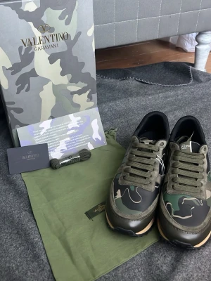 Valentino Garavani Rockrunner sneakers - Säljer ett par Valentino Garavani Rockrunner sneakers i camouflage-mönster. Skorna har gröna, svarta och beige toner, snörning och detaljer i mocka och skinn. Sulan är svart med grovt mönster och bakkappan har nitar. Kommer med extra skosnören och dustbag.