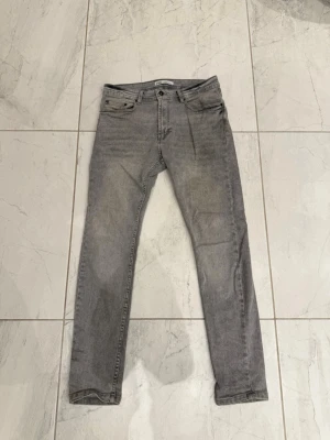 Grå jeans från Zara - Snygga grå jeans från Zara i klassisk femficksmodell. Jeansen har en smal passform och är tillverkade i mjukt denimtyg. Perfekta för dig som gillar en stilren och enkel look.