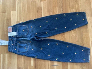 Blå broderade jeans Scotch & Soda - Unika blå jeans från Scotch & Soda med broderade små persikor över hela byxan. Klassisk femficksmodell i bomull med raka ben och normal passform. Perfekta för dig som vill sticka ut med en cool detalj i vardagslooken.