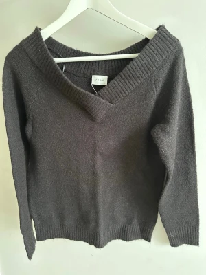 Svart stickad tröja från Vila storlek S-Ny! - Mysig svart stickad tröja från Vila med bred v-ringning och ribbade muddar. Tröjan har lång ärm och är tillverkad i ett mjukt material som passar perfekt till kyligare dagar. Enkel och stilren design som är lätt att matcha.