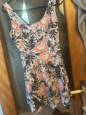 Blommig kortklänning i bomull - Supersöt kortklänning med blommigt mönster i rosa, lila och vitt. Klänningen har ärmlös design, rundad halsringning och lätt utställd kjol. Perfekt för varma dagar och ger en fräsch och somrig vibe. Tillverkad i mjuk bomull för skön komfort.