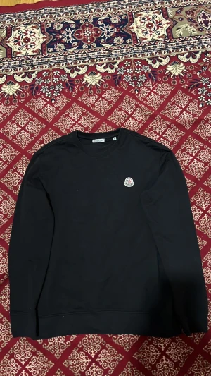 Svart sweatshirt från Moncler - Säljer en svart sweatshirt från Moncler med rund halsringning och Moncler-logga broderad på bröstet. Tröjan har en enkel och clean design med långa ärmar och mjukt material som känns skönt mot huden.